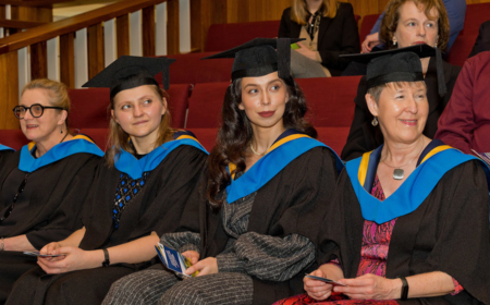 Four alumnae at their graduation, wearing UCD graduation caps and gowns.